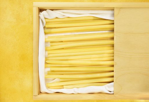 Dlicious  Italian pasta called ziti in a wooden box on yellow table ,long empty tube with smooth side 