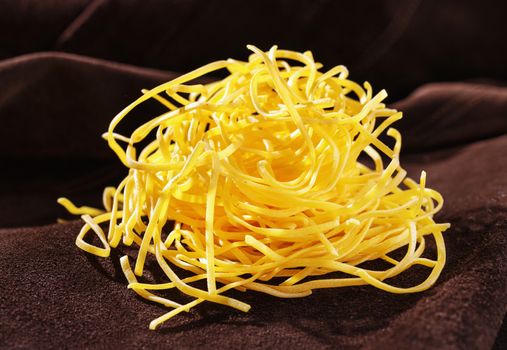 Uncooked pasta fettuccine on colored background , yellow flat thick pasta made with egg and flour