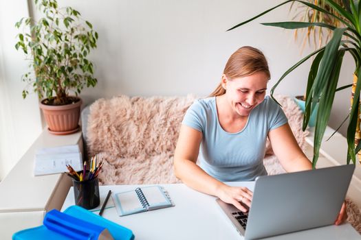 Middle age woman sitting at the table at home working using computer laptop. Work from home and stay at home during coronovirus pandemic concept