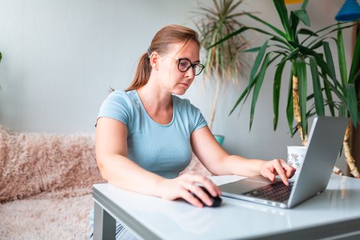 Middle age woman sitting at the table at home working using computer laptop. Work from home and stay at home during coronovirus pandemic concept