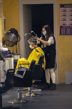 terni,italy september 02 2020:hairdresser who gives hair to a client with medical masks