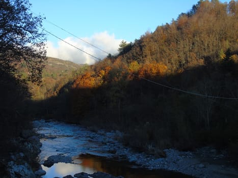 Liguria, Italy -  11/02/2020: Colorful autumn landscape around the village of Tiglieto near the city of Genova. Beautiful sunset reflection in the river and clear blue sky.