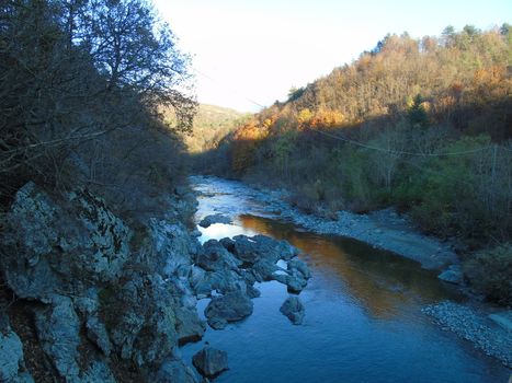 Liguria, Italy -  11/02/2020: Colorful autumn landscape around the village of Tiglieto near the city of Genova. Beautiful sunset reflection in the river and clear blue sky.