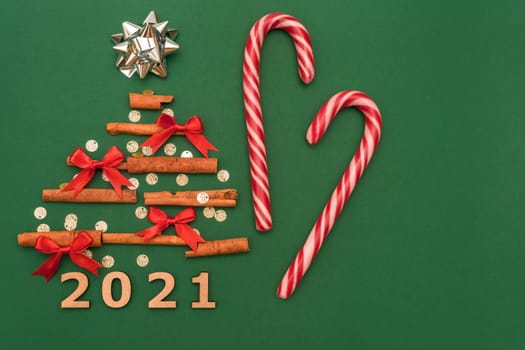 Christmas composition 2021 cinnamon tree, red bows, candy, Christmas cane candies on a green background. Christmas, winter, new year concept. Flat lay, top view, copy space