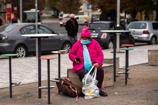 Woman carrying a mask resting with heavy bags during quarantine period due to outbreak of COVID-19 as winter is starting. Prague, Czech Republic