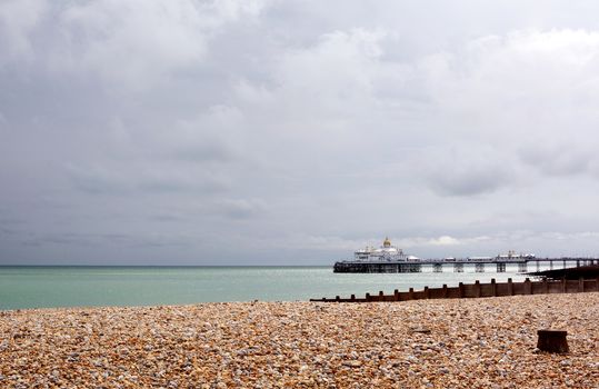 View across shingle beach to Eastbourne pier on the English coast, with stormy summer skies