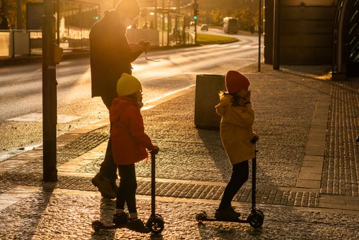 Father and two daughters with mask are crossing the street at Hradcanska metro station with scooters during quarantine period due to outbreak of COVID-19 as winter is starting. Prague, Czech Republic