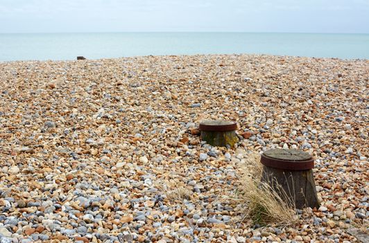 Shingle beach on the English coast with wooden groyne tops emerging from the grey and brown stones