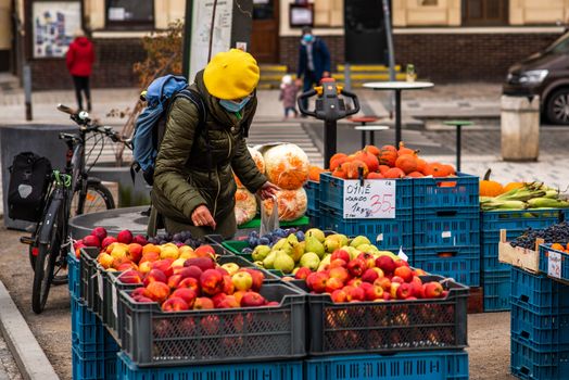 Middle age woman with mask is purchasing fruits and vegetables at the local market during quarantine period due to outbreak of COVID-19 as winter is starting, on an autumn day on Prague 6, Czech republic