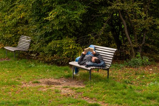 Man is laying on a bench while reading a book on Letna Park in Autumn 2020 on Prague 6 during quarantine period due to outbreak of COVID-19 as winter is starting, Czech Republic