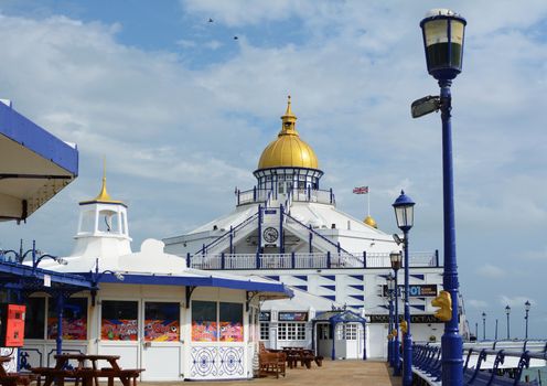 Open deck of Eastbourne pier with seating and arcade entertainment. Gold dome of the pier's tower shines in the sunlight. 