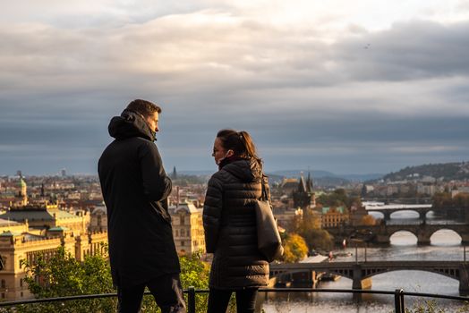 Man and woman are walking and talking on Letna Park while having a spectacular view of the city center in Autumn 2020 on Prague 6, during quarantine period due to outbreak of COVID-19 as winter is starting, Czech Republic
