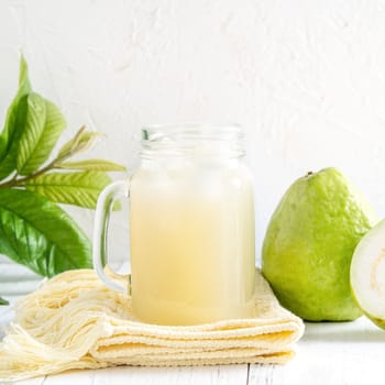 Delicious beautiful guava fruit with fresh juice set isolated on bright white wooden table background, close up.