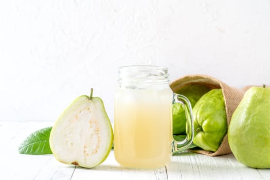 Delicious beautiful guava fruit with fresh juice set isolated on bright white wooden table background, close up.
