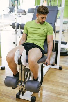 Young sportsman almost shouting when doing leg extension with heavy weight