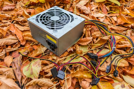 A dump of old computer equipment among which lies a broken power supply in autumn foliage