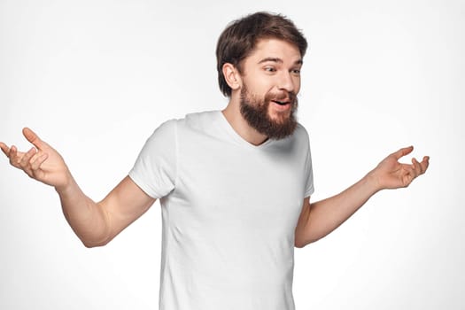 Bearded man in white t-shirt gesture with hands emotions light background. High quality photo