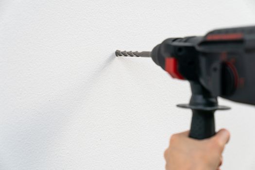 Close up builder or worker hand drilling with a machine on white wall.
