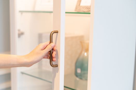 Closeup hand open cupboard display cabinet with glass doors.