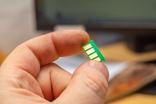 close up, microchip with copper contacts in the hand of a person on the background of a monitor, computer