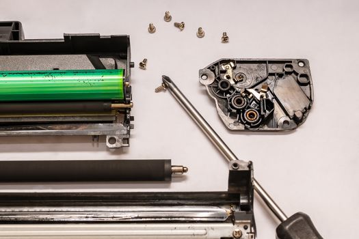 a set of components of the disassembled laser toner cartridge, screwdriver and bolts, lies on a light white surface