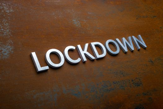 the word lockdown laid with silver metal letters on flat rusted sheet steel background in slanted diagonal perspective with selective focus.