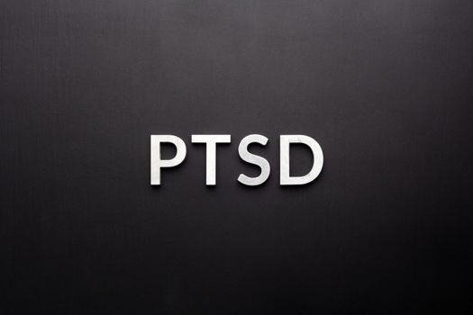 the word PTSD - post traumatic stress disorder - laid with silver metal letters on flat black background in directly above perspective