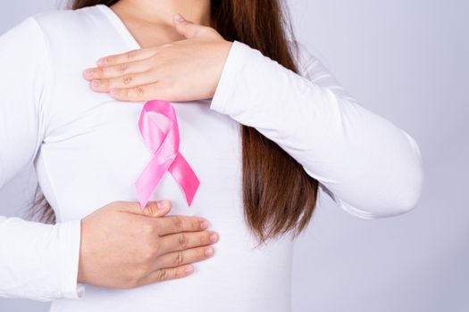 Breast cancer awareness ribbon on woman chest and doing self exam on grey background. Medical, healthcare for advertising concept.