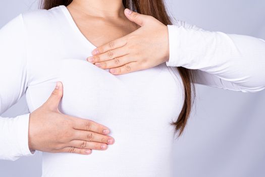 Woman hands doing breast self exam for checking lumps and signs of breast cancer on grey background. Medical, healthcare for advertising concept.
