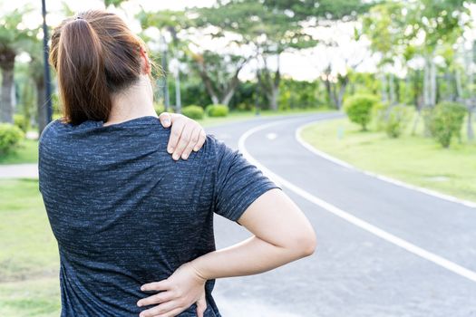 A female athlete suffering from neck and back pain at the park. Injury from sport and exercise concept.