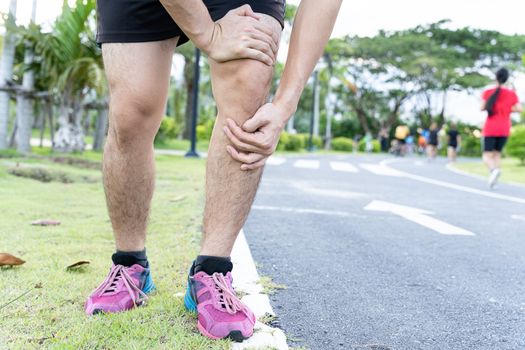 Asian man use hands hold on his knee injury while running on road in the park, Injury from workout concept.