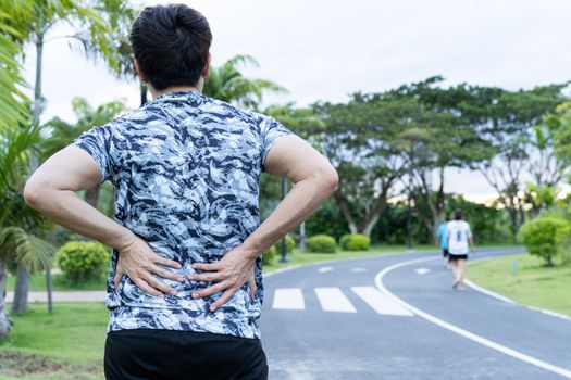 A male athlete suffering from back pain at the park. Injury from sport and exercise concept.