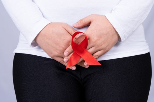 Woman hands holding her crotch with Red AIDS awareness ribbon on grey background. Medical, healthcare for advertising concept.