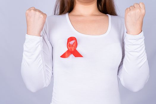 Red AIDS awareness ribbon on woman chest and raise her hand to fight them on grey background. World Aids Day, Healthcare and medical concept.