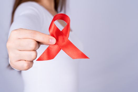 Red AIDS awareness ribbon holding by woman on grey background. World Aids Day, Healthcare and medical concept.
