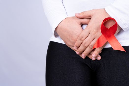Woman hands holding her crotch with Red AIDS awareness ribbon on grey background. Medical, healthcare for advertising concept.