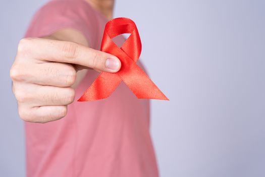 Red AIDS awareness ribbon holding by man on grey background. World Aids Day, Healthcare and medical concept.