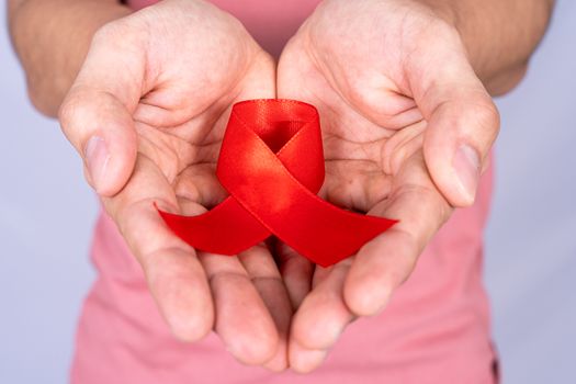Red AIDS awareness ribbon holding by man on grey background. World Aids Day, Healthcare and medical concept.