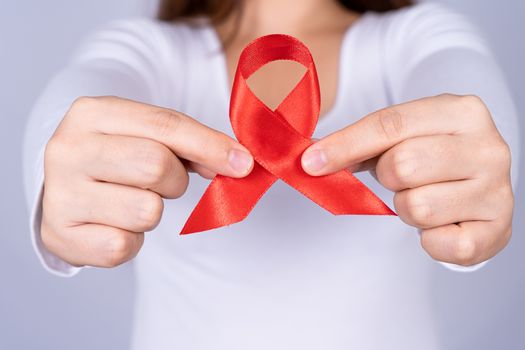 Red AIDS awareness ribbon holding by woman on grey background. World Aids Day, Healthcare and medical concept.