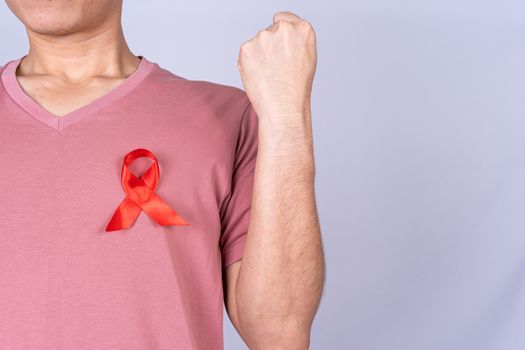 Red AIDS awareness ribbon on man chest and raise his hand to fight them on grey background. World Aids Day, Healthcare and medical concept.