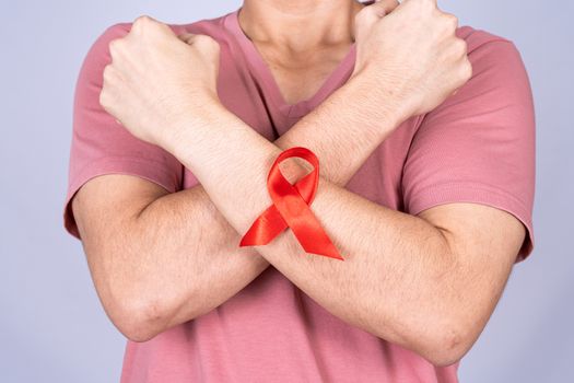Red AIDS awareness ribbon on man arm and raise his hand to fight them on grey background. World Aids Day, Healthcare and medical concept.