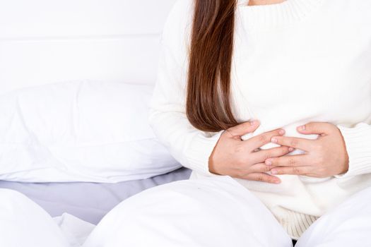 Young woman suffering stomach aches lying on the bed. Healthcare medical or daily life concept.