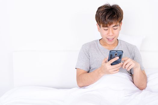 Happy Asian man using a mobile phone lying on the bed at home. Social and technology concept.