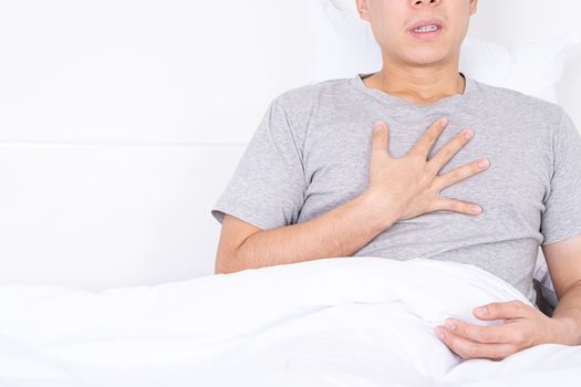 Young man suffering from chest pain after wake up on the bed. Healthcare medical or daily life concept.