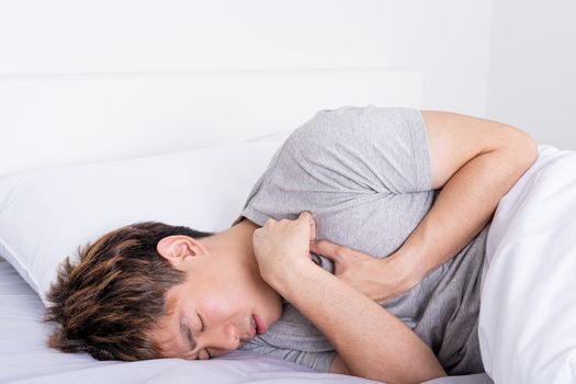 Young man suffering from chest pain after wake up on the bed. Healthcare medical or daily life concept.