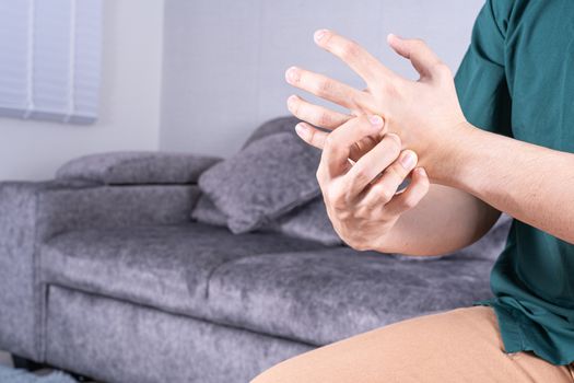 Young man suffering from hand pain while sitting on sofa at home. Healthcare medical or daily life concept.