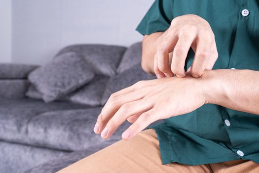 Young man scratching his hand while sitting on sofa at home. Healthcare medical or daily life concept.