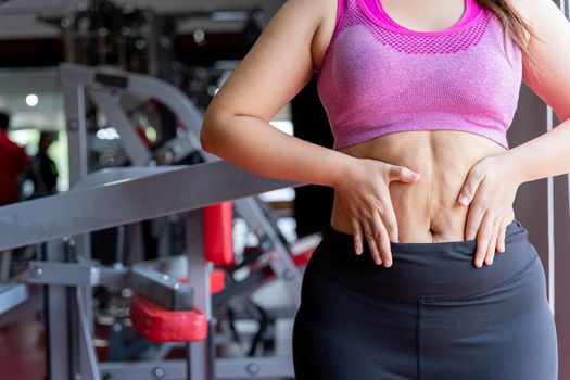 Fat woman holding excessive fat belly, overweight fatty belly at fitness gym. Diet lifestyle, weight loss, stomach muscle, healthy concept.