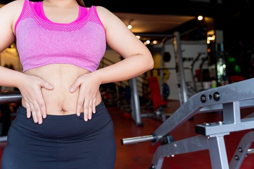 Fat woman holding excessive fat belly, overweight fatty belly at fitness gym. Diet lifestyle, weight loss, stomach muscle, healthy concept.