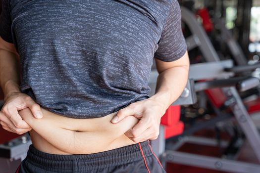 Fat man holding excessive fat belly, overweight fatty belly at fitness gym. Diet lifestyle, weight loss, stomach muscle, healthy concept.